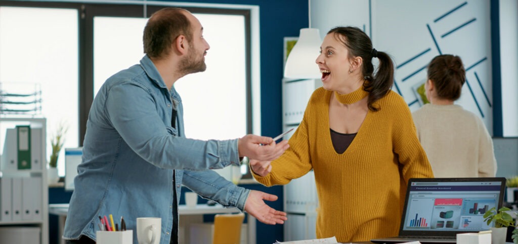 Two colleagues excitedly talking to each other in their office, with visible expressions of happiness.