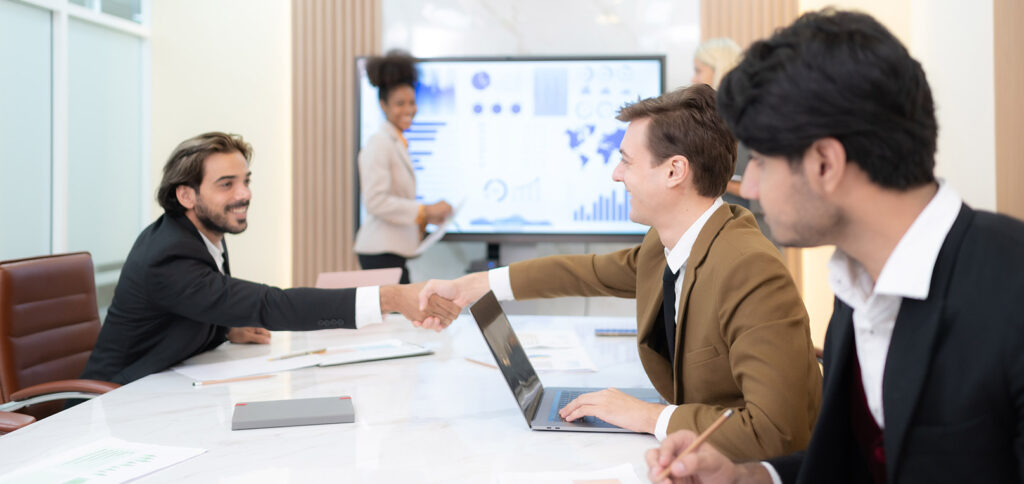 People in a meeting smiling and shaking hands, displaying a pleasant and positive atmosphere.