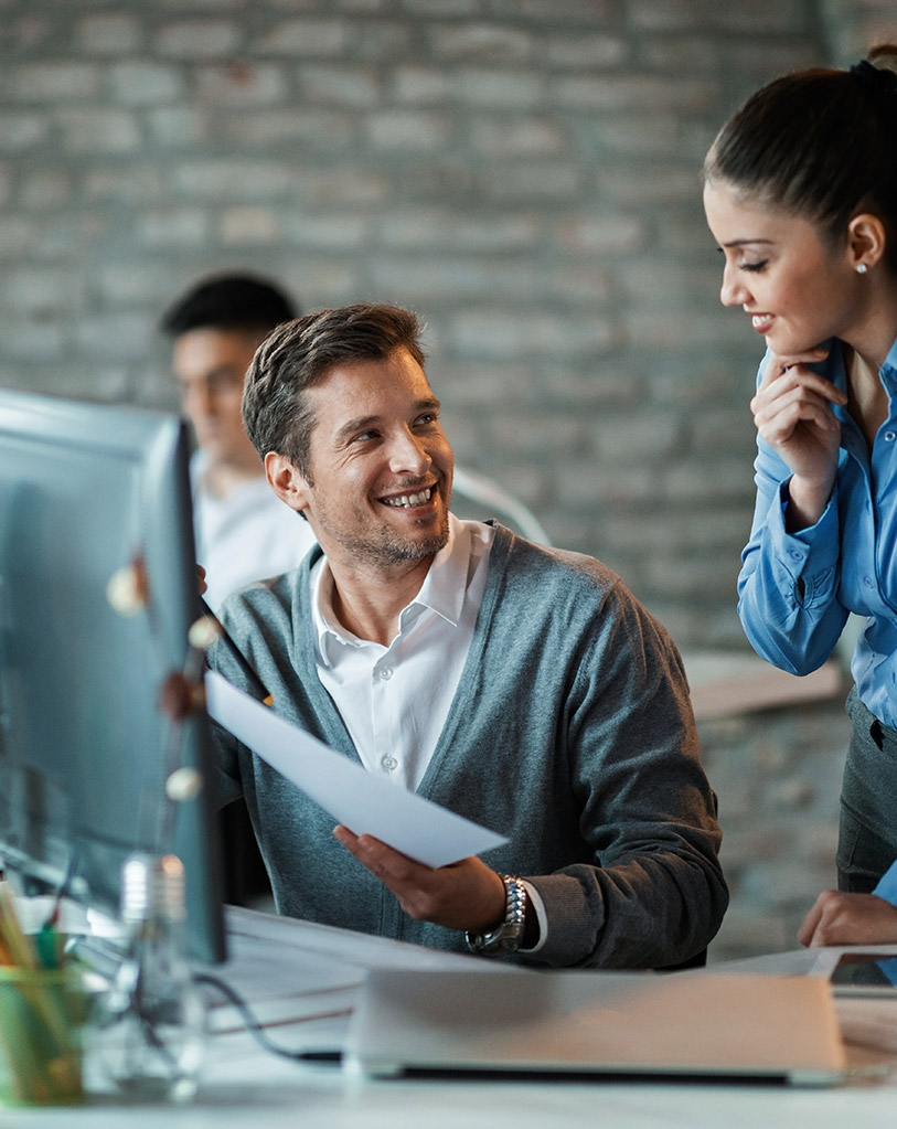 Two smiling colleagues engaging in a friendly conversation in a bright office space.